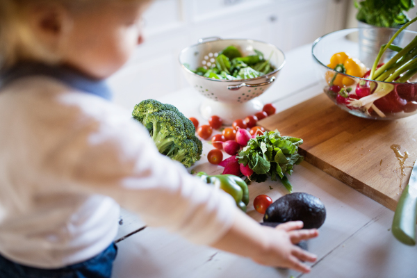 Toddler boy in the kitchen. A small boy sitting on a table with vegetables.