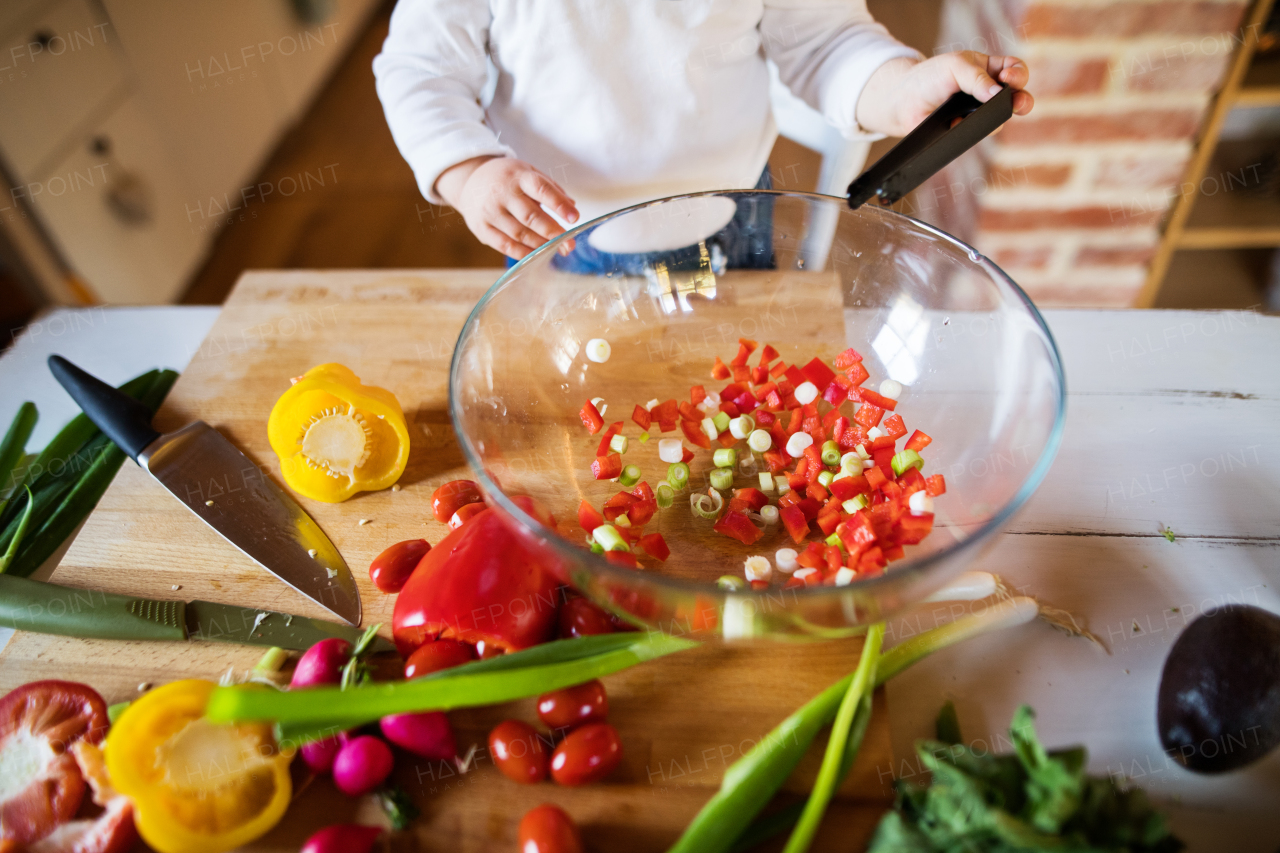 Unrecognizable toddler boy in the kitchen. A small boy making a vegetable salad.