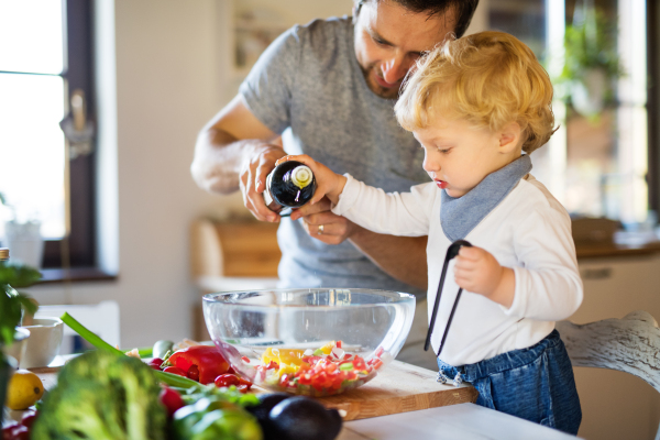 Young father with a toddler boy cooking. A man with his son making vegetable salad.