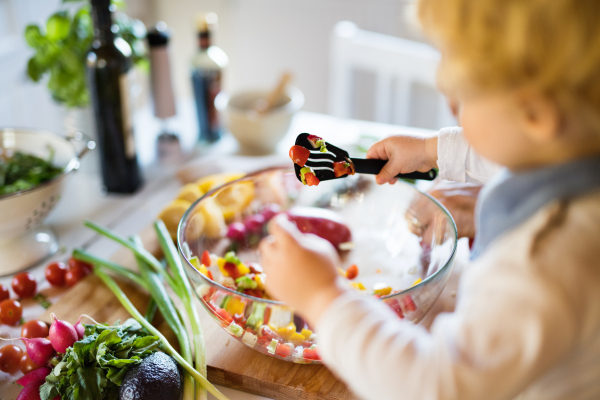 Unrecognizable young father with a toddler boy cooking. A man with his son making vegetable salad.