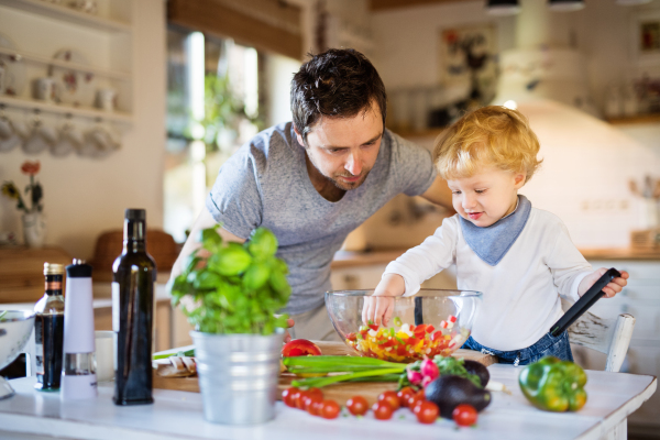 Young father with a toddler boy cooking. A man with his son making vegetable salad.