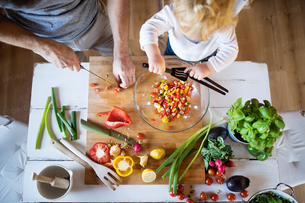 Unrecognizable father with a toddler boy cooking. A man with his son making vegetable salad. Top view.