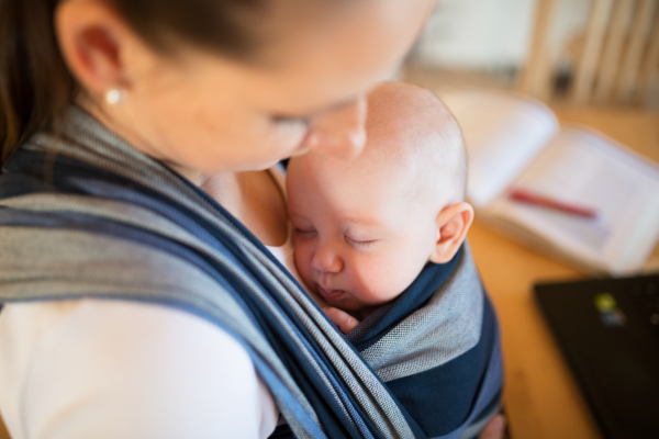 Close up of unrecognizable young mother at home with her baby son sleeping in sling