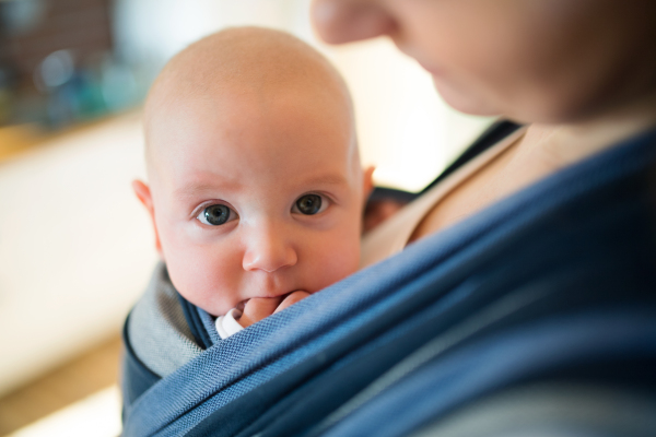 Unrecognizable young mother at home with her baby son in sling