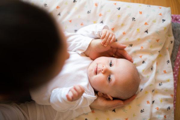 Unrecognizable mother caressing her cute baby son lying on a blanket.