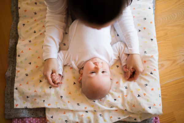 Unrecognizable mother holding hands of her cute baby son lying on a blanket.