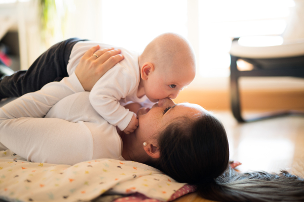 Beautiful mother lying on the floor, holding her cute baby son, biting her nose