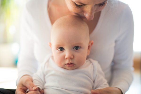 Unrecognizable mother in white t-shirt holding her cute baby son, sitting in her lap.