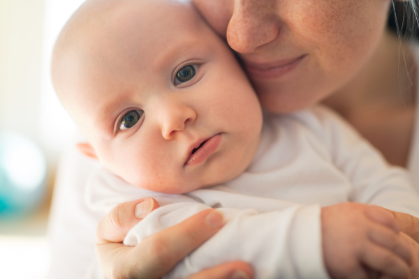 Unrecognizable mother in white t-shirt holding her cute baby son, sitting in her lap.