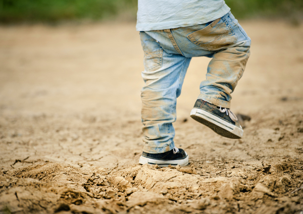 Cute toddler boy making first steps on the field road, summer time.