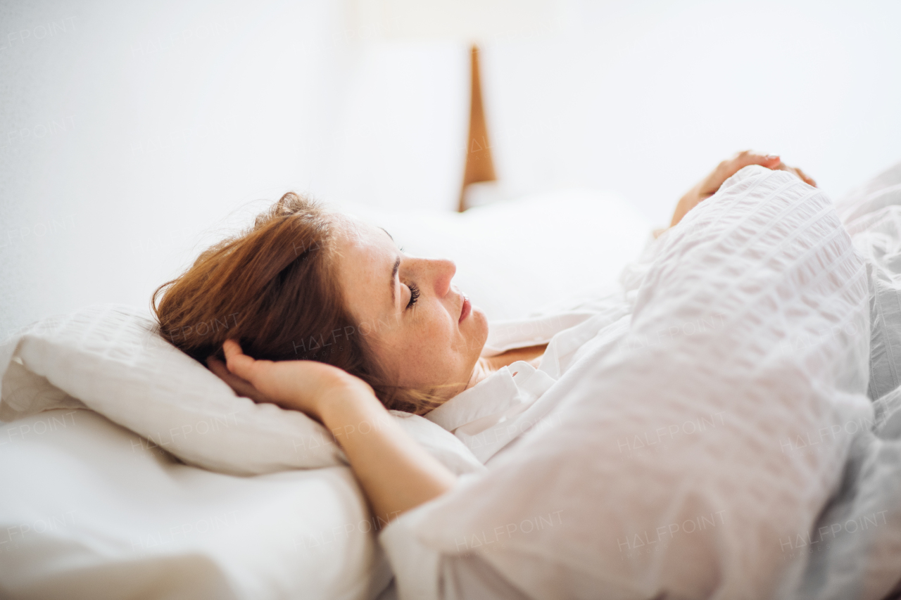 A happy young woman lying in bed indoors in the morning in a bedroom, sleeping.