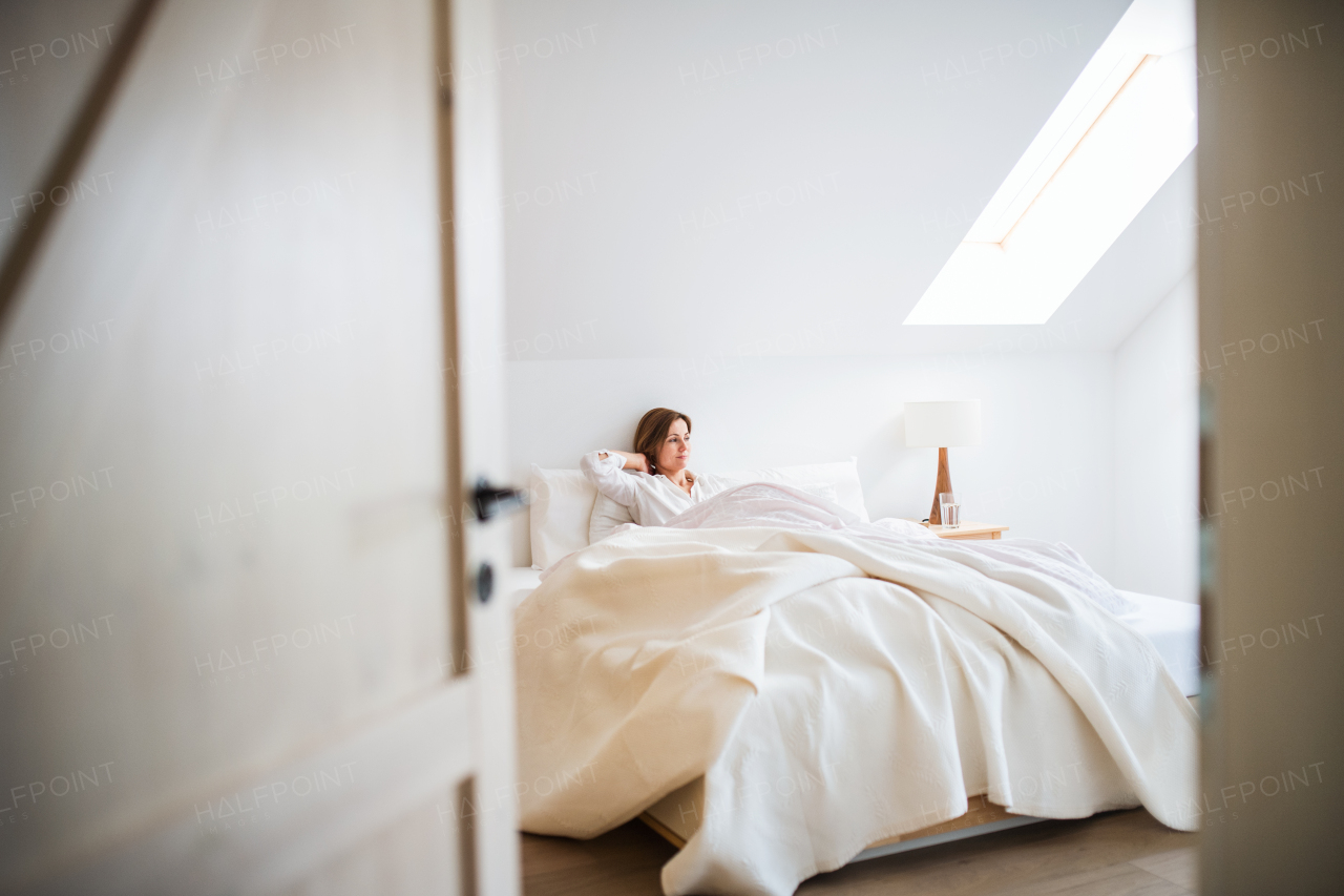 A happy young woman sitting in bed indoors in the morning in a bedroom, resting.