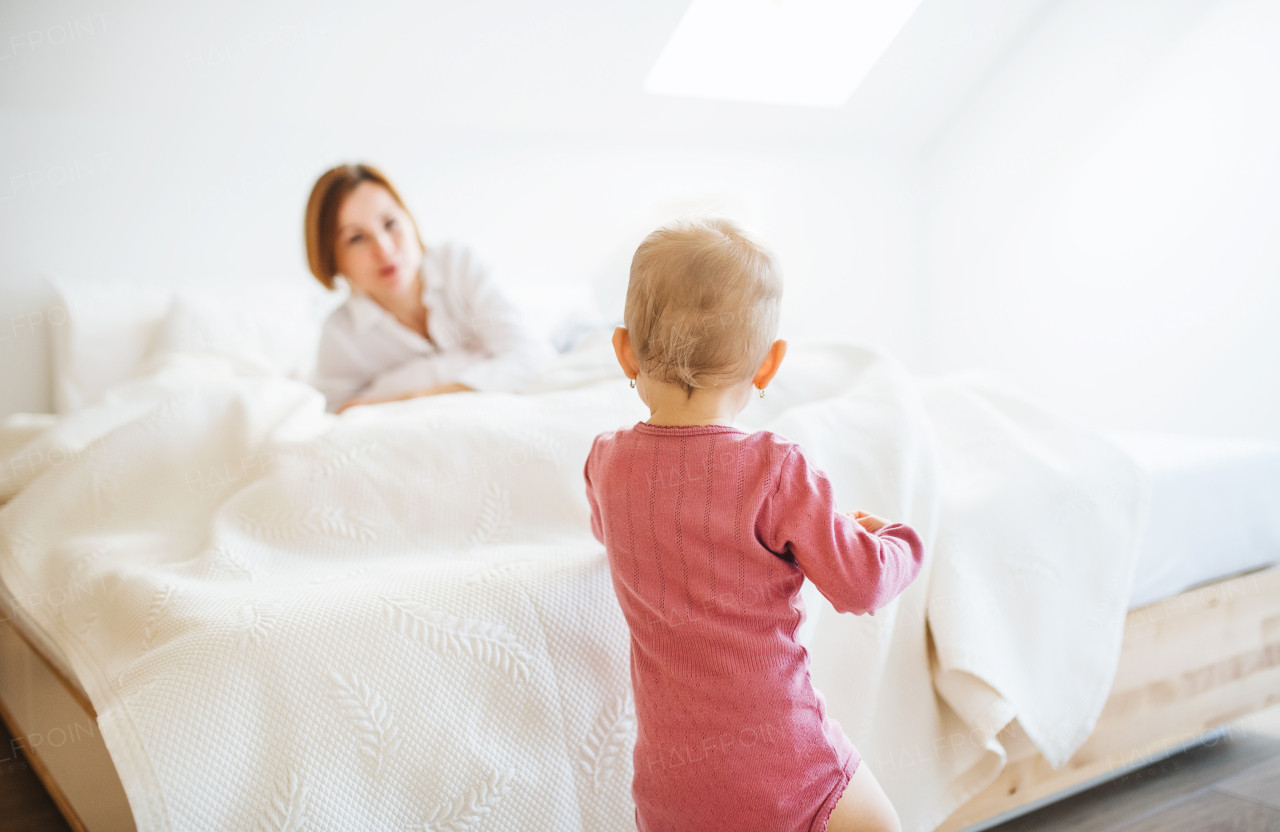 A happy young mother with little daughter indoors on bed in the morning, playing.