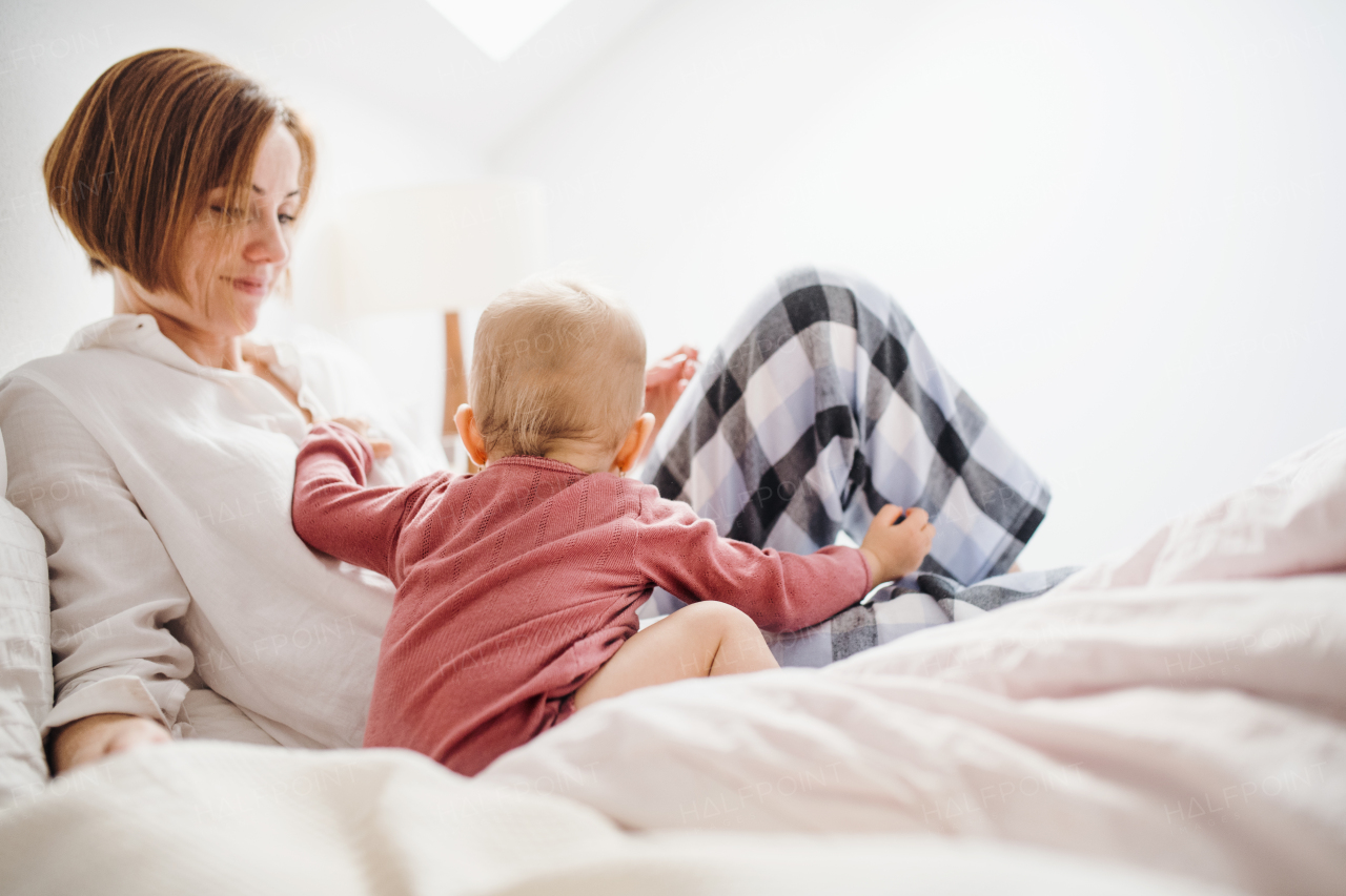 A happy young mother with little daughter sitting indoors on bed in the morning, playing.