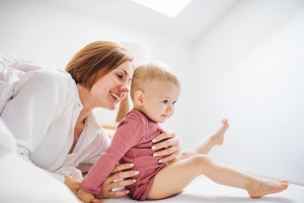 A happy young mother with little daughter sitting indoors on bed in the morning, playing.