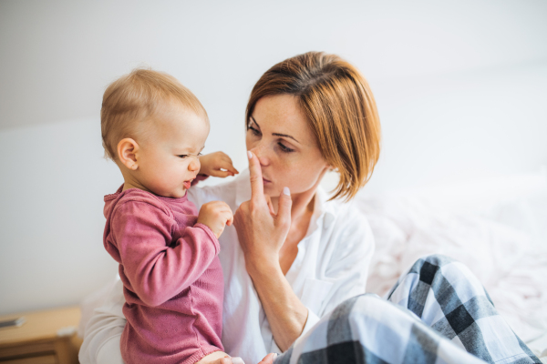 A happy young mother with little daughter sitting indoors on bed in the morning, playing.