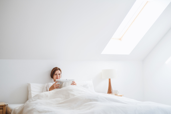 A morning routine of young woman reading newspapers in bed in a bedroom.