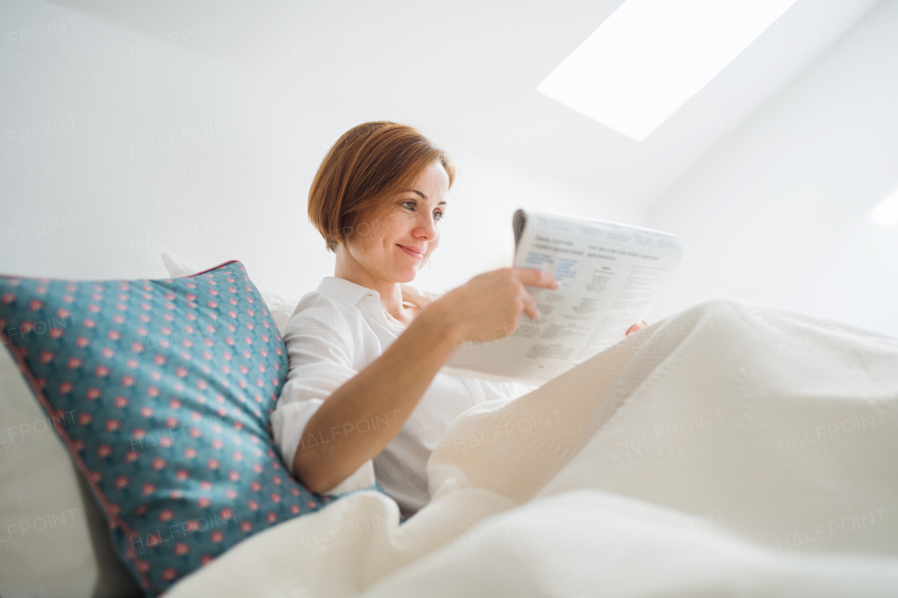 A morning routine of young woman reading newspapers in bed in a bedroom.