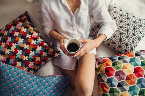 A midsection view of young woman with night shirt sitting indoors on bed in the morning.