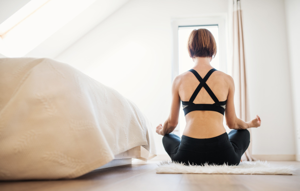 A rear view of young woman doing yoga exercise indoors in a bedroom. Copy space.