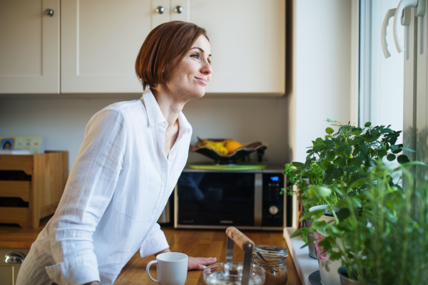 A happy young woman looking out of a window in the kitchen.