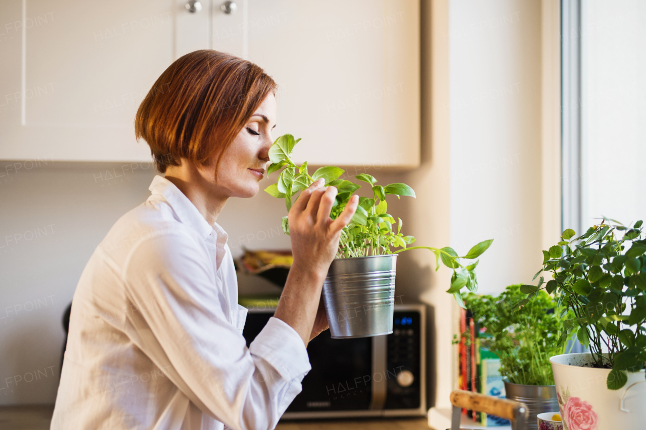 A young woman with closed eyes standing indoors in kitchen, smelling herbs.