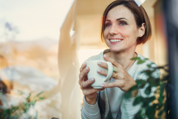 A young woman with cup of coffee looking out of a window. Shot through glass. A copy space.