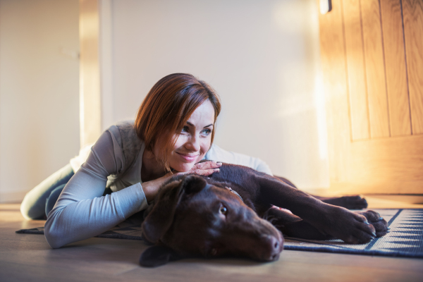 A happy young woman lying indoors on the floor at home, playing with a dog.