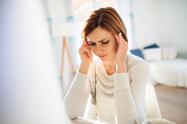 A sad young woman in pain sitting indoors, working in a home office.