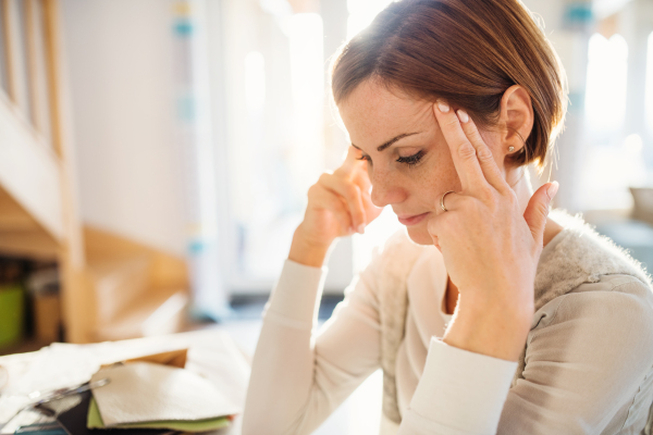 A thoughtful young woman sitting at a desk indoors, working in a home office.