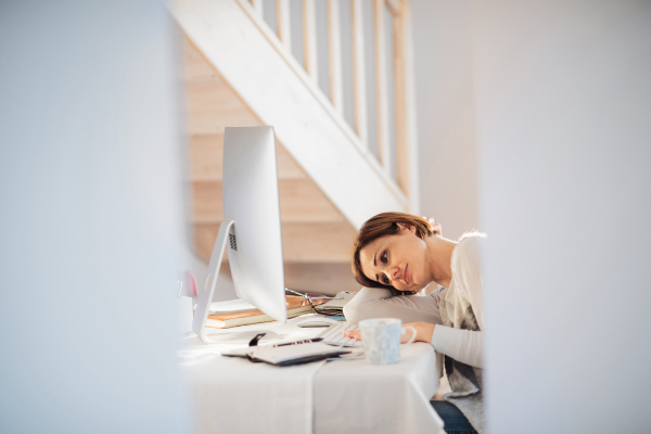 A tired young woman sitting indoors, working in a home office.