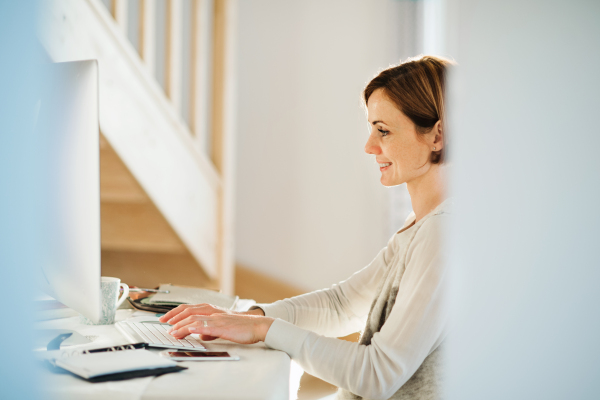 A happy young woman sitting indoors, working in a home office.