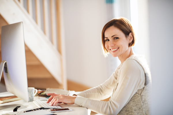 A happy young woman sitting indoors, working in a home office.