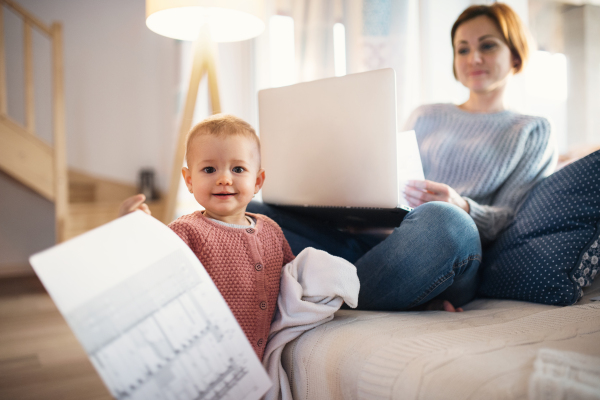 A young woman with a toddler daughter sitting indoors, working at home.