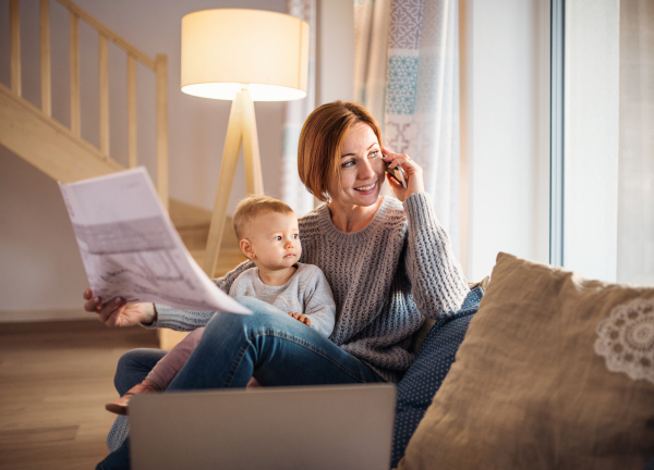 A young woman on the phone with a toddler daughter sitting indoors, working at home.