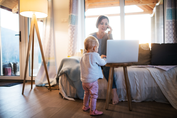 A young woman on the phone with a toddler daughter sitting indoors, working at home.