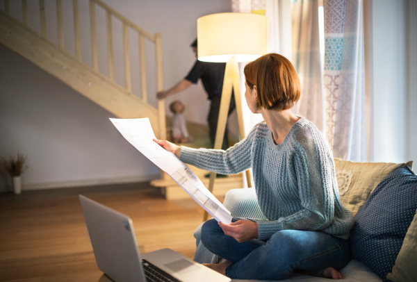 A young woman with laptop and blueprints sitting indoors, working at home.