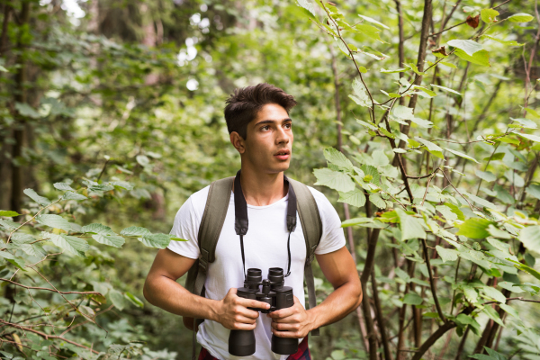 Teenage boy with backpack and binoculars hiking in forest. Summer vacation adventure.