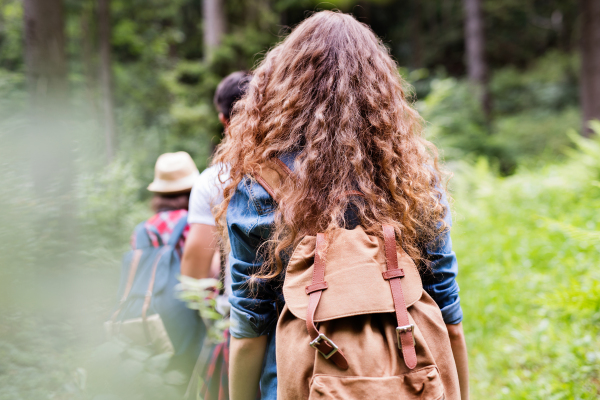 Teenagers with backpacks hiking in forest. Summer vacation adventure.