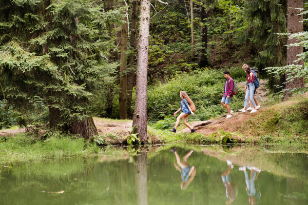 Teenagers with backpacks hiking in forest at the lake. Summer vacation adventure.