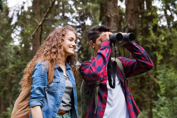 Teenage couple with binoculars hiking in forest. Summer vacation adventure.