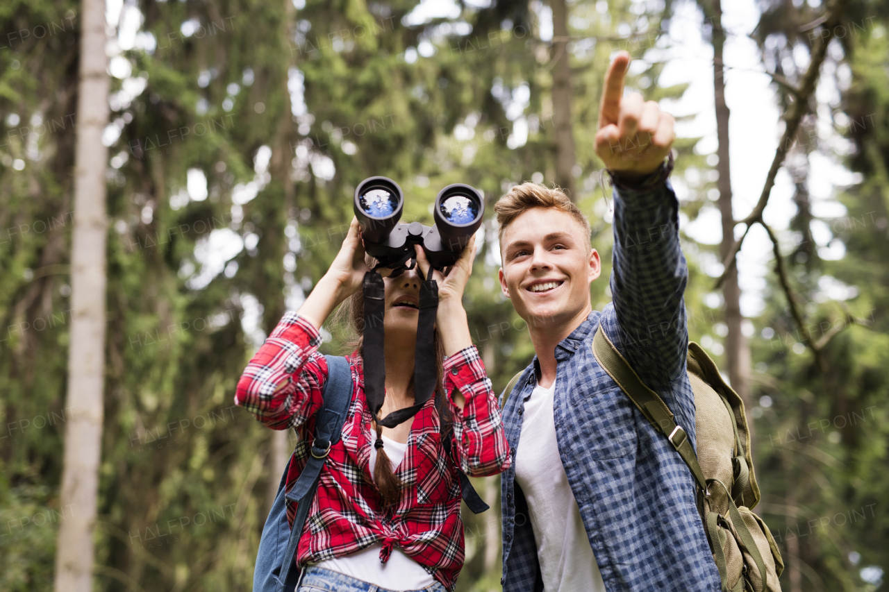 Teenage couple with binoculars hiking in forest. Summer vacation adventure.