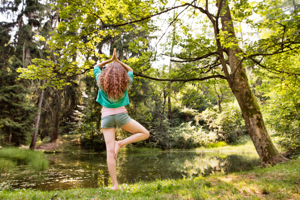 Beautiful girl practices yoga in the morning forest. Young woman sits,relaxes and meditates in nature. Rear view.