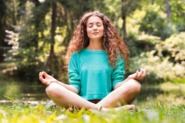 Beautiful teenage girl practices yoga in the morning forest. Young woman sits,relaxes and meditates in nature.