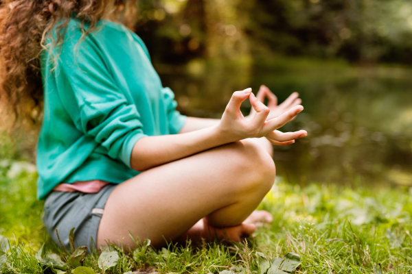 Unrecognizable girl practices yoga in the morning forest. Young woman sits,relaxes and meditates in nature.