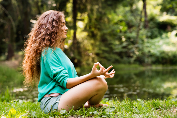 Beautiful teenage girl practices yoga in the morning forest. Young woman sits,relaxes and meditates in nature.