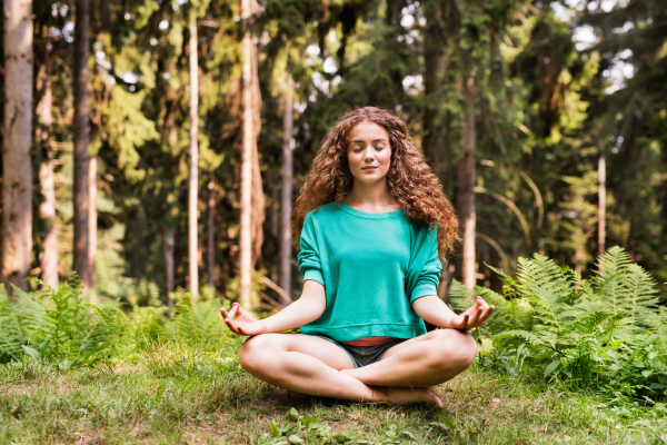 Beautiful teenage girl practices yoga in the morning forest. Young woman sits,relaxes and meditates in nature.