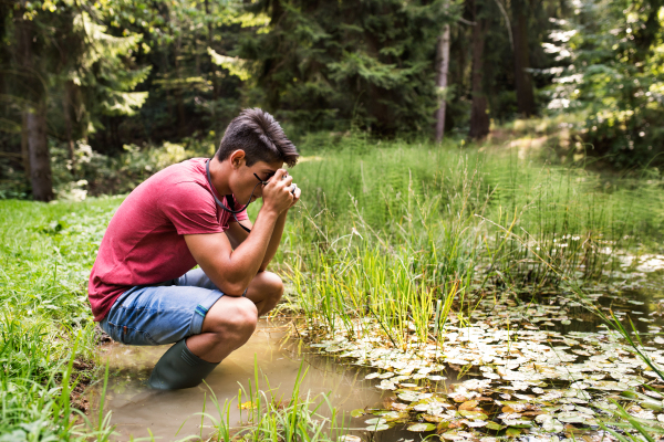 Teenage boy with camera in the lake, taking picture. Summer vacation adventure.