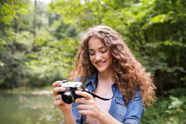 Teenage girl hiking in forest, taking pictures with camera. Summer vacation adventure.