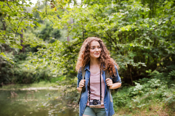 Teenage girl with backpack and camera hiking in forest. Summer vacation adventure.